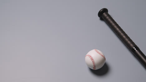 Overhead-Baseball-Still-Life-With-Bat-And-Ball-Rolling-Into-Frame-Against-Grey-Background